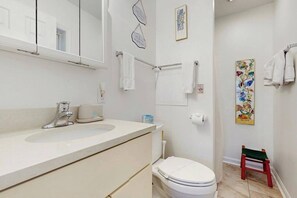 Un baño con lavamanos blanco, inodoro y un taburete de madera.