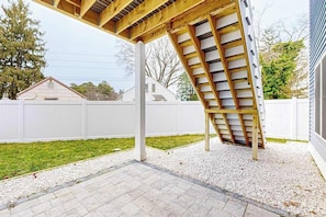 A covered patio area with a wooden beam structure, a white fence, and a gravel ground. - Spacious townhouse w/patio, balcony, WIFI, W/D (Rehoboth Beach)
