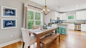 Une cuisine moderne avec des meubles blancs, une table à manger en bois et un lustre.