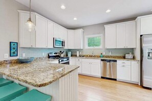 A kitchen with white cabinets, granite countertops, a stainless steel refrigerator, and a window with a view. - Town of Rehoboth Beach cottage with covered porch, deck, grill, AC, & W/D (Rehoboth Beach)
