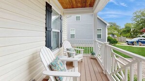 Une véranda avec deux fauteuils Adirondack blancs, un plafond en bois et une balustrade blanche.