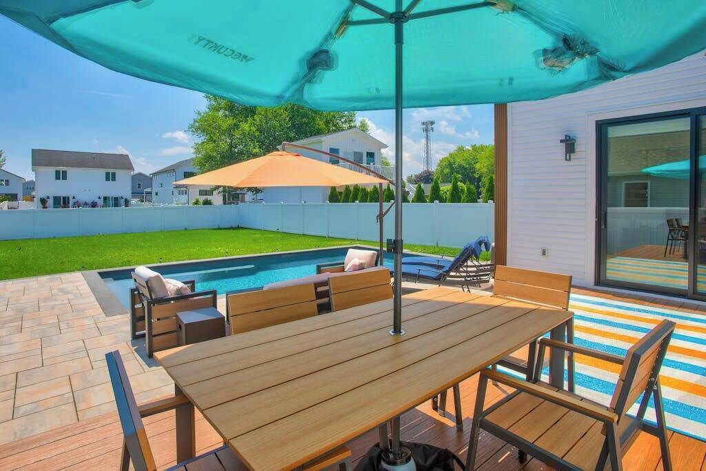 An outdoor patio with a pool, wooden furniture, and umbrellas.