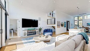 Uma sala de estar moderna com uma TV de tela plana, um sofá, uma mesa de centro e uma escada que leva a um andar superior.