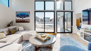 Uma sala de estar moderna com uma janela grande, um sofá, uma mesa de centro e uma pintura de uma árvore.