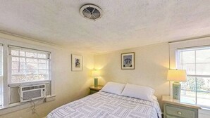A bedroom with a bed, two bedside tables with lamps, a window with blinds, and a ceiling vent.