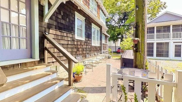 A wooden house with a porch, outdoor seating, and a white fence.