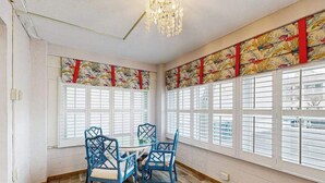 Una habitación con una mesa redonda, cuatro sillas, ventanas amplias con contraventanas y una araña.