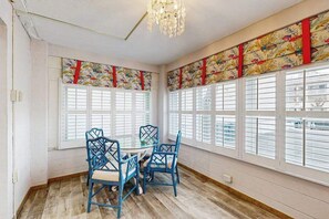 Ein Zimmer mit einem runden Tisch, vier Stühlen, großen Fenstern mit Fensterläden und einer Deckenleuchte.