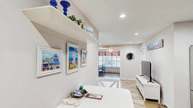 Un interior moderno con un mostrador de recepción blanco, cuadros enmarcados en la pared, un televisor y una escalera que conduce a otra habitación.