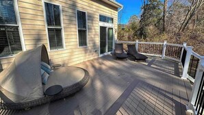A deck with outdoor seating, a railing, and a house in the background. - Grande at Canal Pointe home with pools, sports courts, & gym (Rehoboth Beach)