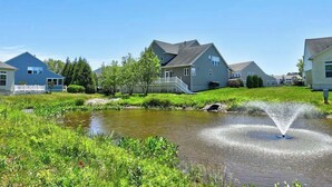 A residential area with houses, a pond, and a fountain. - Grande at Canal Pointe home with pools, sports courts, & gym (Rehoboth Beach)
