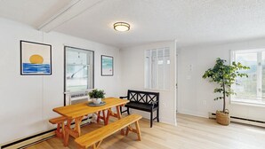 Una habitación con una mesa de madera y bancos, una planta en maceta y una ventana con persianas.