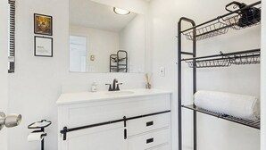 Un baño con lavamanos, espejo, toallero y un mueble blanco con cajones.