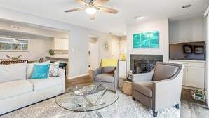 A modern living room with a ceiling fan, a glass coffee table, a sofa, two armchairs, a fireplace, and a TV. - Eagles Landing - updated condo w/two balconies, WiFi, W/D, & AC - great location (Rehoboth Beach)