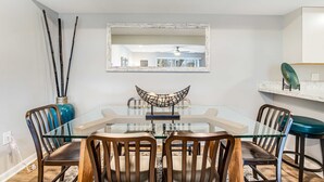 A dining area with a glass table, wooden chairs, and a decorative bowl centerpiece. - Eagles Landing - updated condo w/two balconies, WiFi, W/D, & AC - great location (Rehoboth Beach)