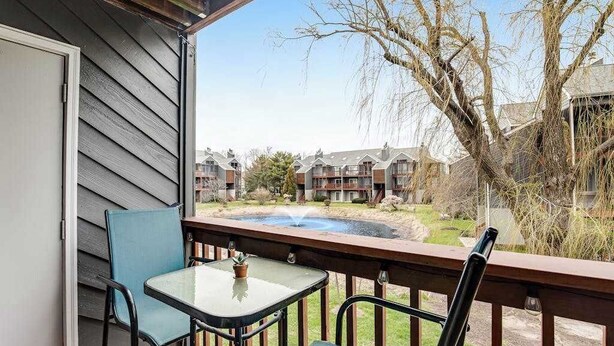 A balcony with a table and chairs, overlooking a courtyard with buildings and a water feature. - Eagles Landing - updated condo w/two balconies, WiFi, W/D, & AC - great location (Rehoboth Beach)
