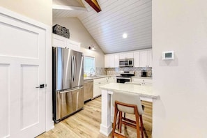 A kitchen with white cabinets, stainless steel appliances, a wooden floor, and a white island with bar stools.