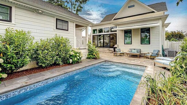 Une maison à deux étages avec une piscine, un espace salon extérieur et une terrasse couverte.