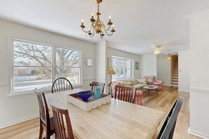 Un comedor amplio con una mesa grande, sillas y una araña. Varias ventanas ofrecen luz natural y vistas al exterior.