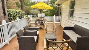 A covered outdoor deck with wicker furniture, a yellow umbrella, and a white fence. - Country Manor dog friendly house w/ping pong, deck & balcony (Rehoboth Beach)