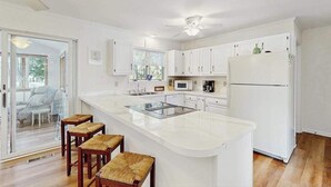 A modern kitchen with white cabinetry, a central island with stools, a ceiling fan, and a refrigerator. - Country Manor dog friendly house w/ping pong, deck & balcony (Rehoboth Beach)