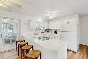 Una cocina moderna con armarios blancos, una isla central con taburetes, un ventilador de techo y un refrigerador.