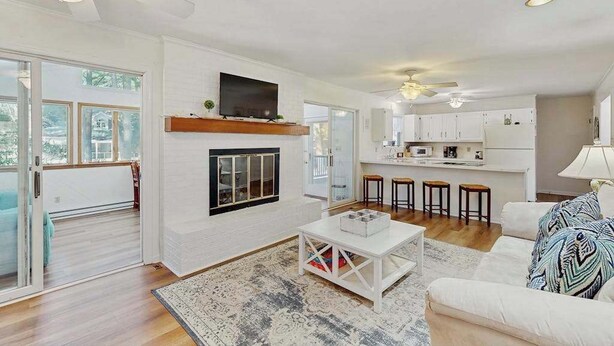 A modern living room with a fireplace, a TV mounted on the wall, and a kitchen area with bar stools. - Country Manor dog friendly house w/ping pong, deck & balcony (Rehoboth Beach)