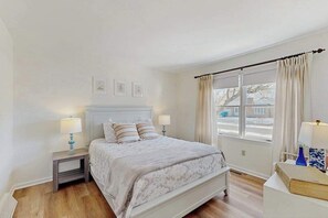 Un dormitorio con cama, mesitas de noche, ventana con cortinas y vistas al exterior.