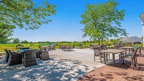 An outdoor patio area with tables and chairs, surrounded by trees and a view of a golf course. - Bear Trap Dunes 2nd-floor, lakefront condo w/ pool and free WiFi - 1 dog OK (Ocean View)