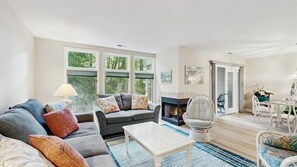 Un salon comprenant un canapé, un fauteuil, une table basse, une cheminée et de grandes fenêtres.