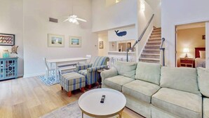 A spacious living room with a sofa, armchairs, a coffee table, and a staircase.