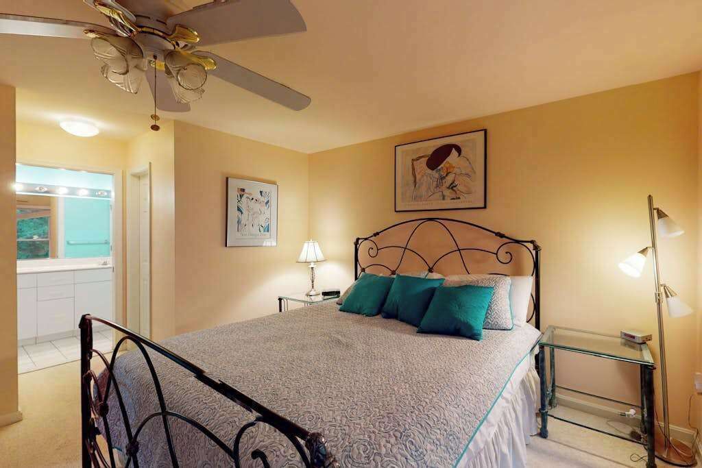 Une chambre à coucher avec un lit, un ventilateur de plafond, des œuvres d’art et une table de chevet.