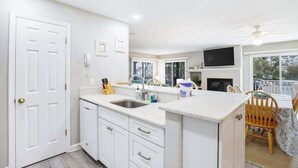 A kitchen with white cabinets, a sink, and a dining area with a table and chairs. - Sea Colony Tennis 1st-floor condo with gym, tennis court, & sauna (Bethany Beach)