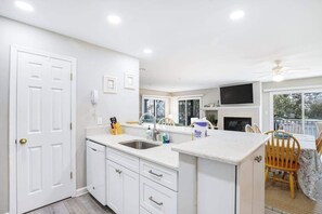 Una cocina con armarios blancos, un lavamanos y una zona de comedor con mesa y sillas.