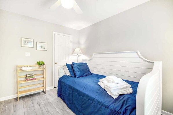 A bedroom with a bed, a bedside table, a lamp, a shelf with books, and a door. - Sea Colony Tennis 1st-floor condo with gym, tennis court, & sauna (Bethany Beach)