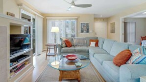 A living room with a television, sofa, glass coffee table, and a ceiling fan. - Sea Colony Tennis 1st-floor condo with sauna, gym, & pool (Bethany Beach)