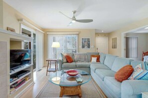Ein Wohnzimmer mit Fernseher, Sofa, Glastisch und Deckenventilator.