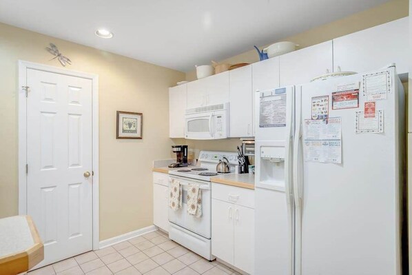 Una cocina compacta con armarios blancos, un microondas, una estufa y un refrigerador.