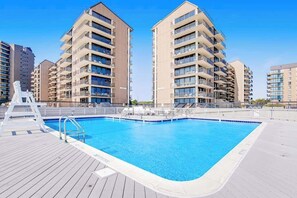 A swimming pool with a wooden deck, surrounded by multi-story residential buildings. - Sea Colony Tennis 2nd-floor condo pool & gym (Bethany Beach)