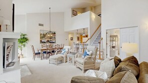 A spacious living room with a fireplace, dining area, and staircase leading to an upper level. - Sea Colony Tennis 2nd-floor condo pool & gym (Bethany Beach)