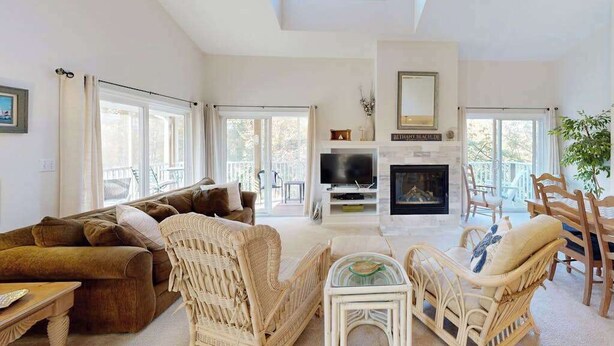 A spacious living room with a fireplace, a television, and wicker furniture. - Sea Colony Tennis 2nd-floor condo pool & gym (Bethany Beach)