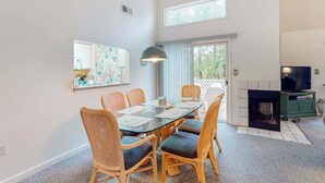 Un comedor con mesa de vidrio, sillas de mimbre, chimenea y televisor.