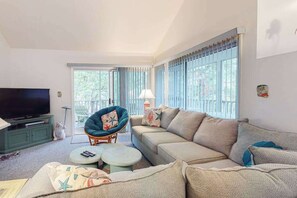 A living room with a sofa, armchair, TV, and a small round table. - Sea Colony Tennis 2nd-floor condo with basketball court, & sauna (Bethany Beach)
