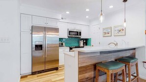 Une cuisine moderne avec des meubles blancs, des appareils en acier inoxydable, un pare-feu turquoise et des tabourets de bar en bois.