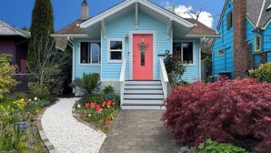 Ein Haus mit roter Tür, einer Veranda und einem Garten mit verschiedenen Pflanzen und Blumen.