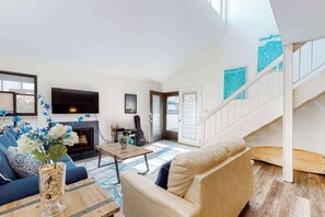 A spacious living area with a sofa, coffee table, and a fireplace. There is a staircase leading to an upper level. - Sea Colony Tennis 1st-floor condo with tennis court, sauna & pool (Bethany Beach)
