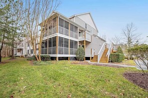 A two-story house with a balcony, a front porch, and a staircase leading to the second floor. - Two-story beach gem with wraparound screened porch, pool, sauna & gym (Bethany Beach)