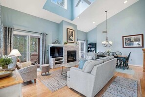 A spacious living room with a fireplace, a dining area, and a seating area with a sofa and chairs. - Two-story beach gem with wraparound screened porch, pool, sauna & gym (Bethany Beach)
