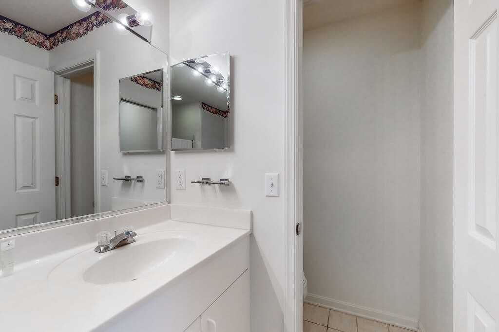 A bathroom with a white sink, a mirror, and a door leading to another room.