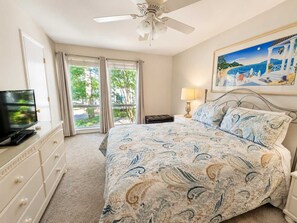 A bedroom with a bed, a television, a ceiling fan, a painting, and a view through the window. - Sea Colony townhouse with Tennis, sauna, basketball court, & pool (Bethany Beach)